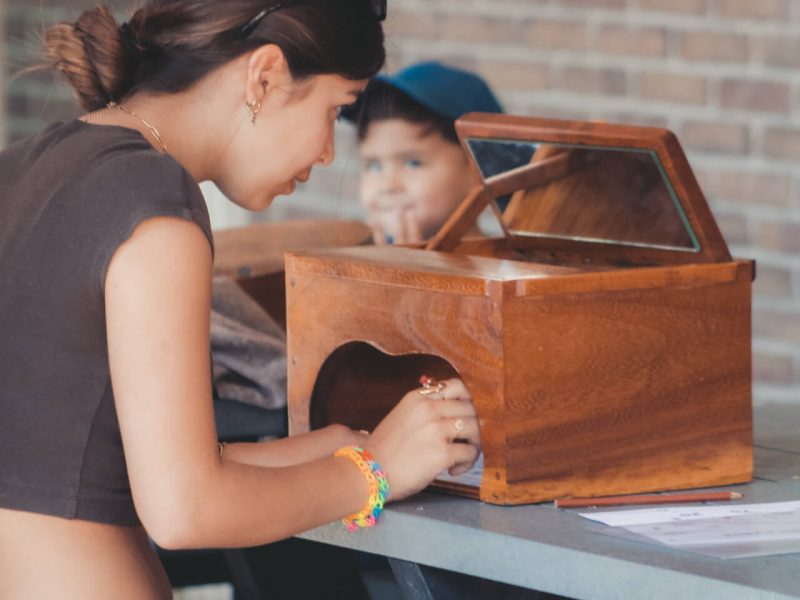 Meisje speelt het traditionele Nederlandse spel spiegelschrijven met een houten spiegelbox. Ze kijkt via de spiegel naar het parcours en tekent het in spiegelbeeld met een pen.