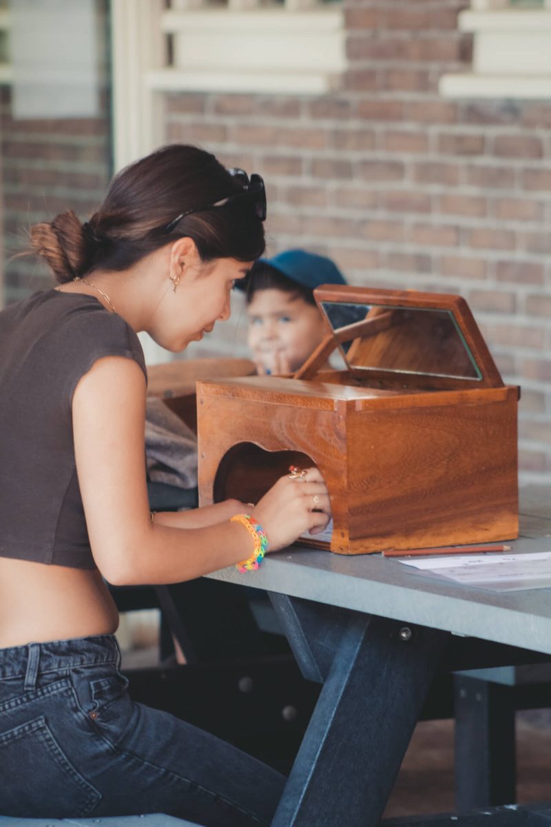 Meisje speelt het traditionele Nederlandse spel spiegelschrijven met een houten spiegelbox. Ze kijkt via de spiegel naar het parcours en tekent het in spiegelbeeld met een pen.