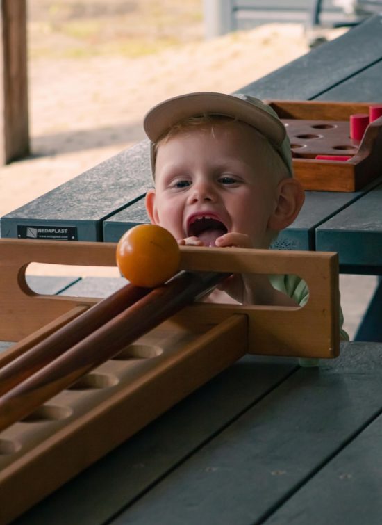 Klein kind speelt blij het traditionele Nederlandse spel trekbiljart aan tafel. Het kind komt net met zijn hoofd boven de tafel uit en bedient het spel.