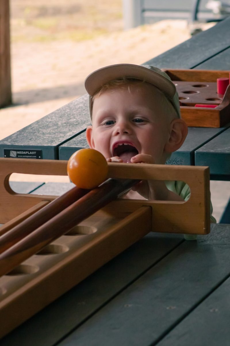 Klein kind speelt blij het traditionele Nederlandse spel trekbiljart aan tafel. Het kind komt net met zijn hoofd boven de tafel uit en bedient het spel.